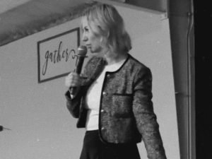 black and whoite photo of woman preaching, one hand on micriphone the other in a pointing direction to the floor. woman is onstage like on the church platform.